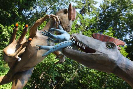 Realistische Dinosaurier-Skulpturen im Saurierpark Kleinwelka: ein Dino beißt in den Hals eines kleineren, ein anderer greift mit Krallen.