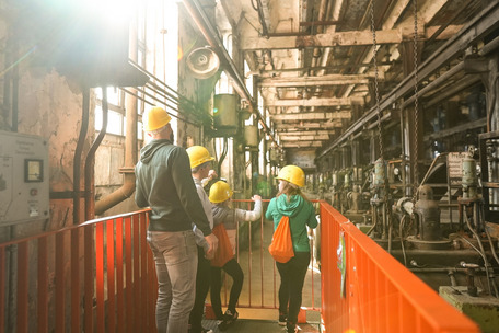 Personengruppe mit Helmen und Warnwesten in Industrieanlage mit Rohren, Maschinen und rotem Geländer – Energiefabrik Knappenrode.