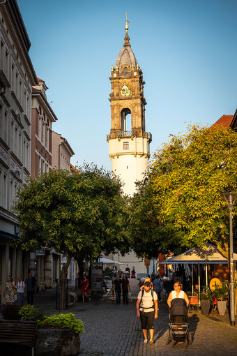 Reichenturm in Bautzen im Zentrum des Bildes, mit Uhr und Architekturdetails, Kopfsteinpflasterstraße, Menschen und Außengastronomie.