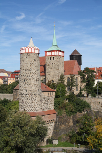 Blick auf die Alte Wasserkunst in Bautzen bei blauem Himmel, umgeben von Bäumen, im Hintergrund historische Gebäude.