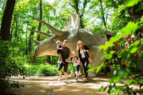 Eine Familie steht im Wald vor einem Dinosaurier
